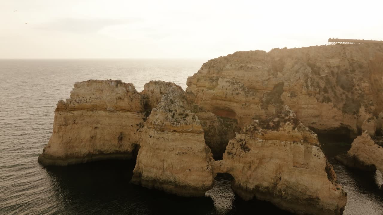 Drone shot above dramatic coastal rock formations with boats navigating between cliffs near the Atlantic Ocean