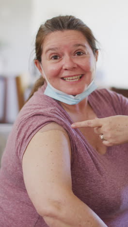 video vertical de una mujer caucásica sonriente que muestra yeso en el brazo después de la vacuna contra el coronavirus