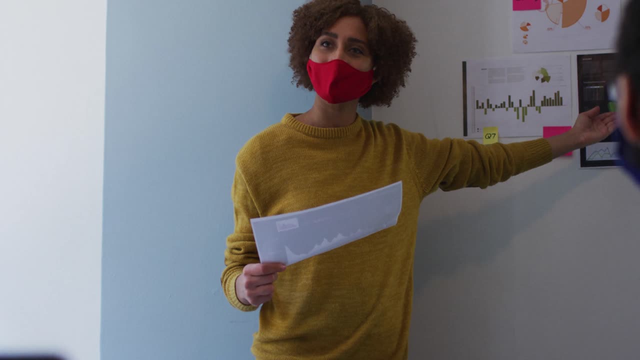 mujer de raza mixta con máscara facial en la oficina dando una presentación