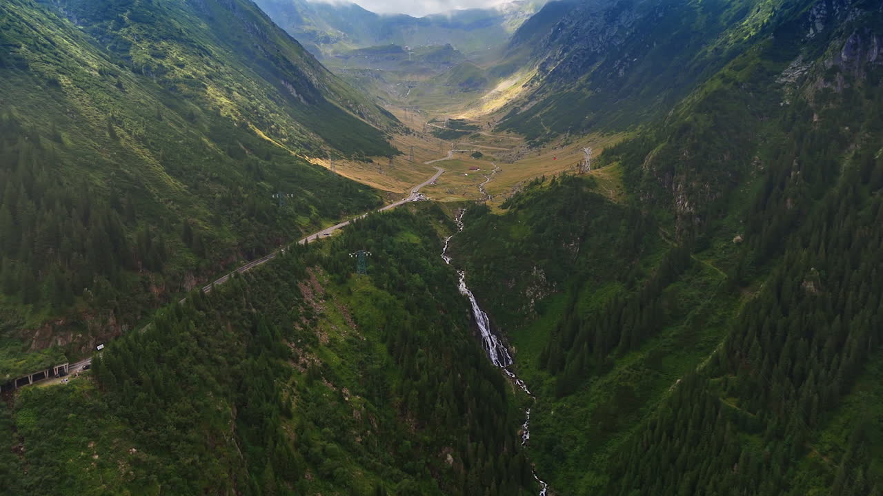 Mountain waterfall in the Romanian Carpathians. A tall waterfall cascades down a deep green valley in the Carpathian Mountains of Romania, viewed from above