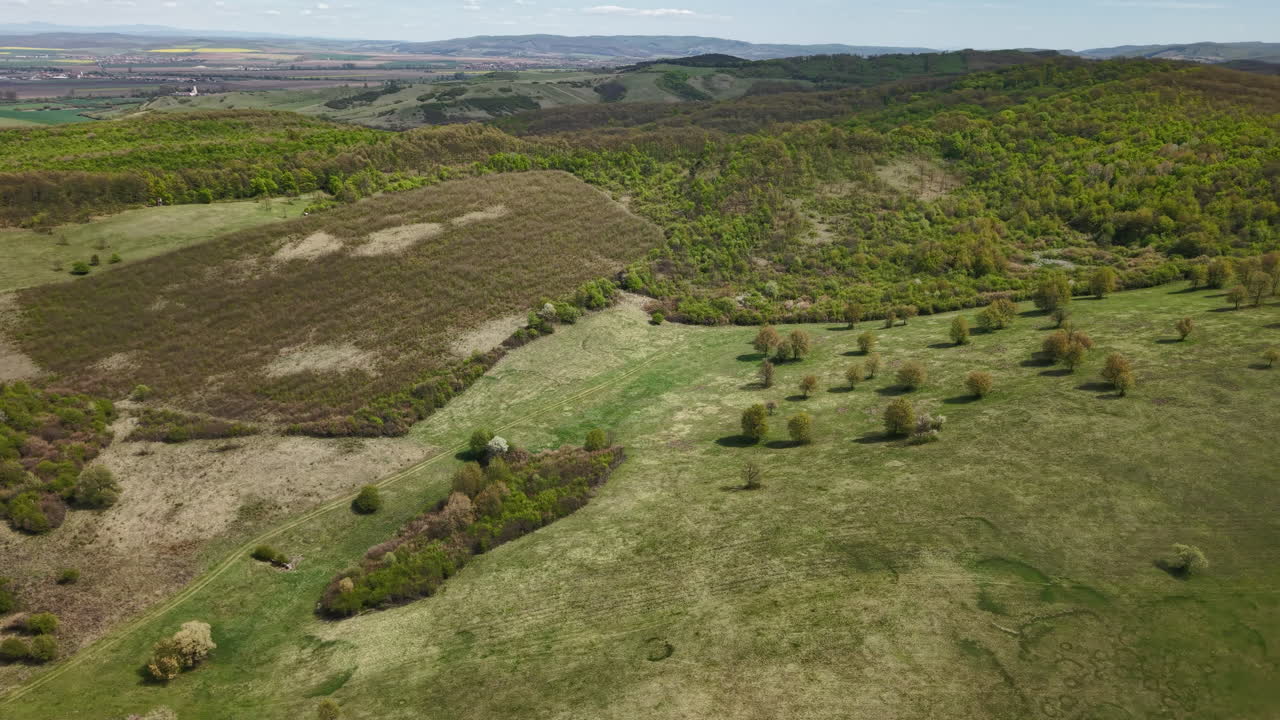 Rozsáhlý letecký pohled z dronu ukazuje svěží zelené kopce a zalesněné plochy pod jasnou oblohou na venkově.