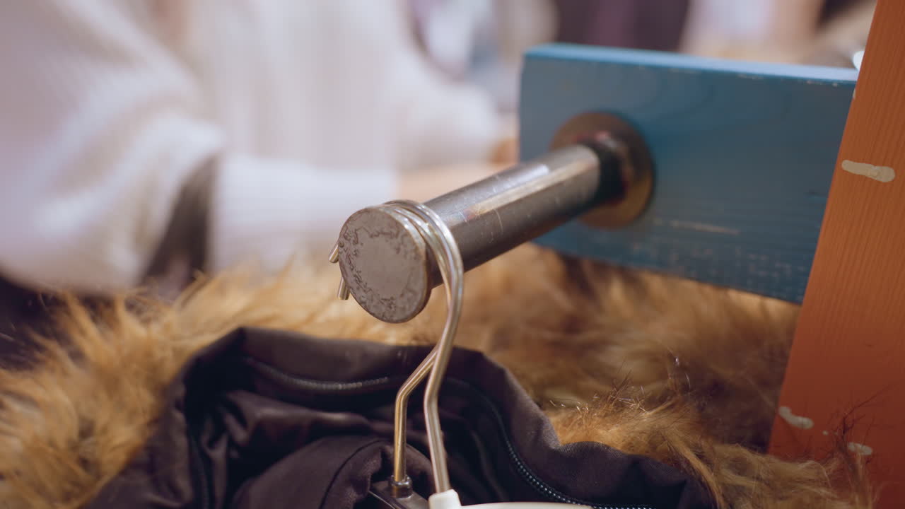 Close up of winter coat hanging on rack with faint hand browsing fur trim under warm boutique lighting among organized apparel racks evoking tactile shopping experience and fabric exploration