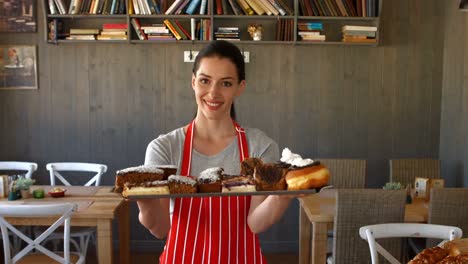 Portrait-of-female-baker-holding-sweet-food-in-tray