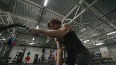 young muscular man performing battle rope workout in gym
