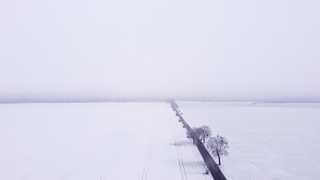 Volando-A-Lo-Largo-De-Un-Camino-Recto-Que-Atraviesa-Tierras-De-Cultivo-Cubiertas-De-Nieve