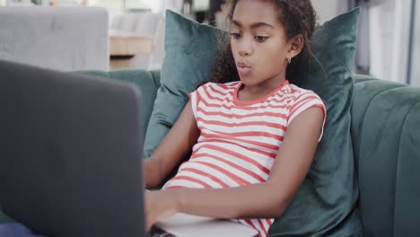 una feliz chica afroamericana sentada en el sofá, usando una computadora portátil, cámara lenta