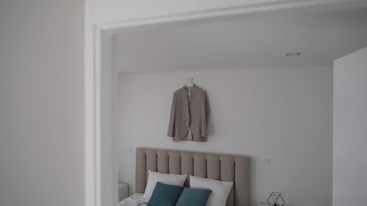 blazer bronceado colgado en una pared en un dormitorio moderno con almohadas de azul azulado y una decoración neutral