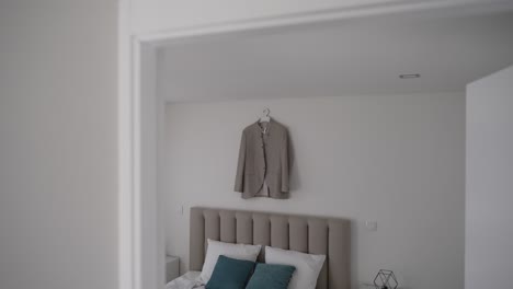 tan blazer hanging on a wall in a modern bedroom with teal pillows and a neutral decor
