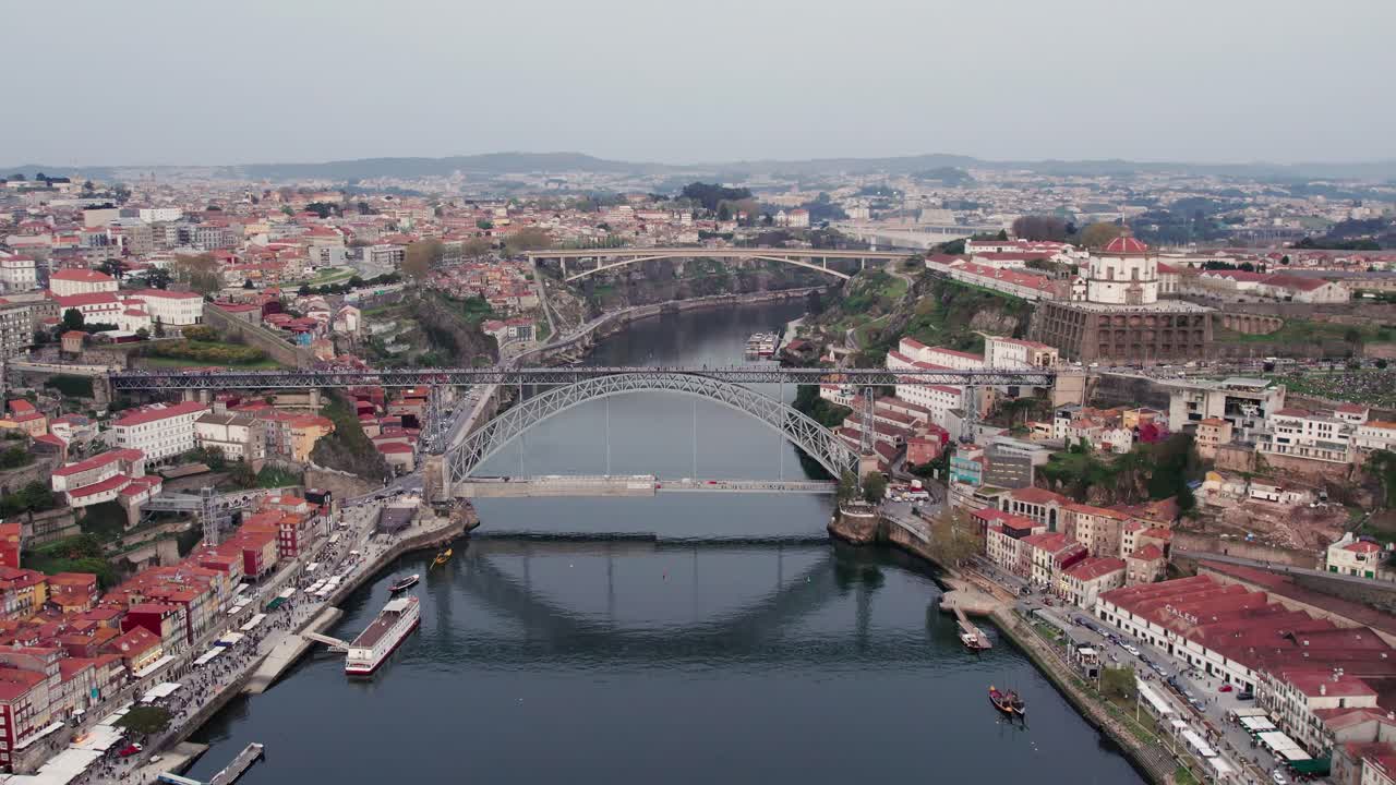 Porto, Portugal, presenting a wide aerial view of the cityscape, featuring the iconic Dom Luis I Bridge crossing the Douro River, historic buildings and a vibrant waterfront along the riverbanks