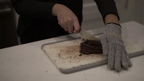 una niña corta chocolate negro antes de derretirlo para hacer galletas de mantequilla millonarias mientras usa guantes de seguridad-3