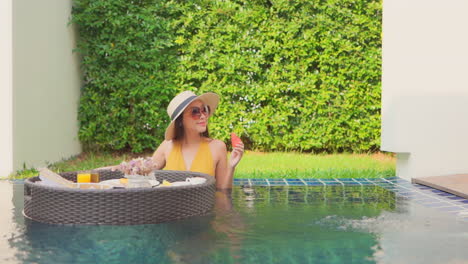 healthy asian woman in mustard color bathing suit enjoying her breakfast on a floating tray in a private pool