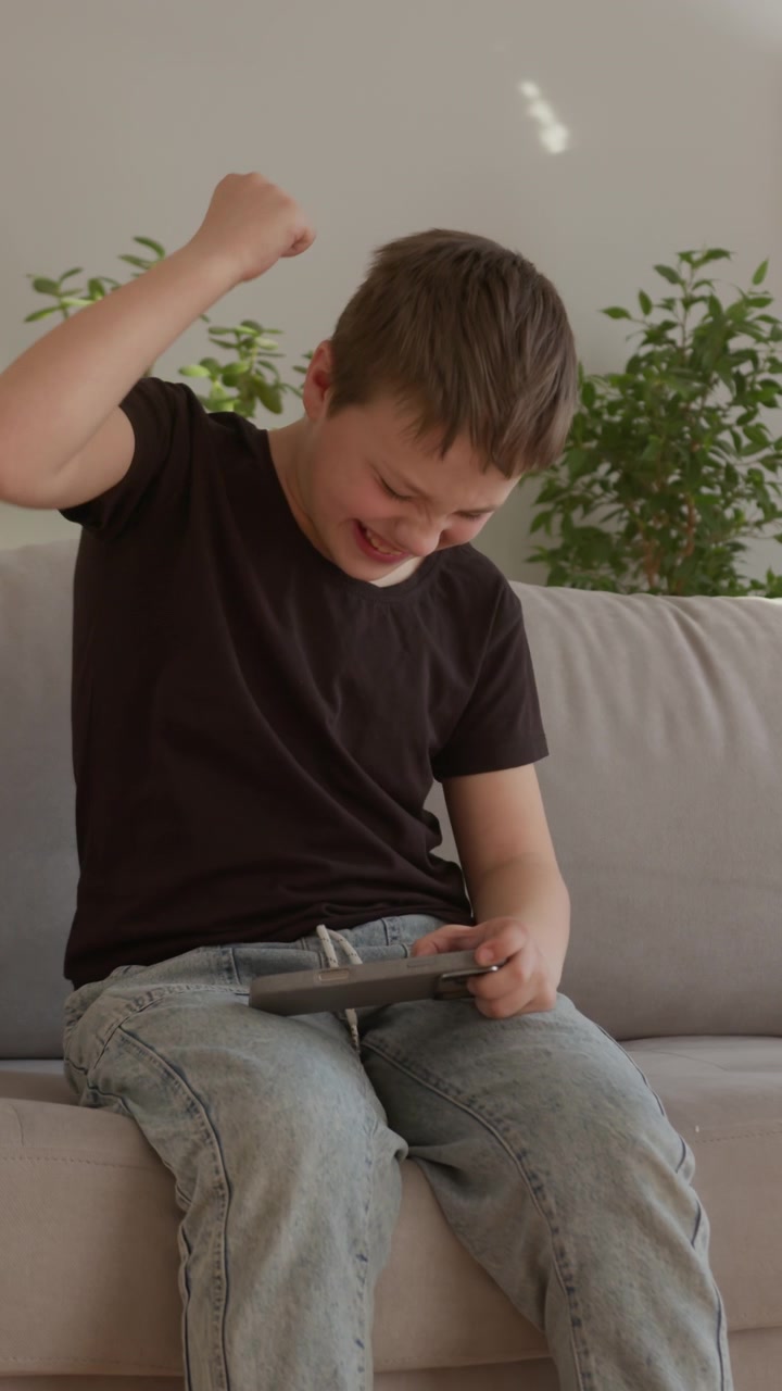 Young boy sits on couch playing video game with intense emotions showing frustration and