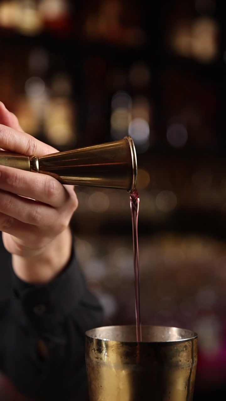 Barman che versa liquido dosato da un misurino in uno shaker da cocktail