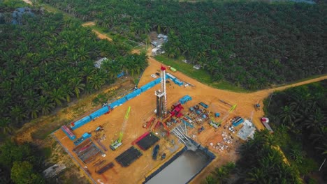 cinematic onshore drilling and workover rig structure and rig equipment for oil exploration and exploitation in the middle of jungle surrounded by palm oil trees during sunset time.
