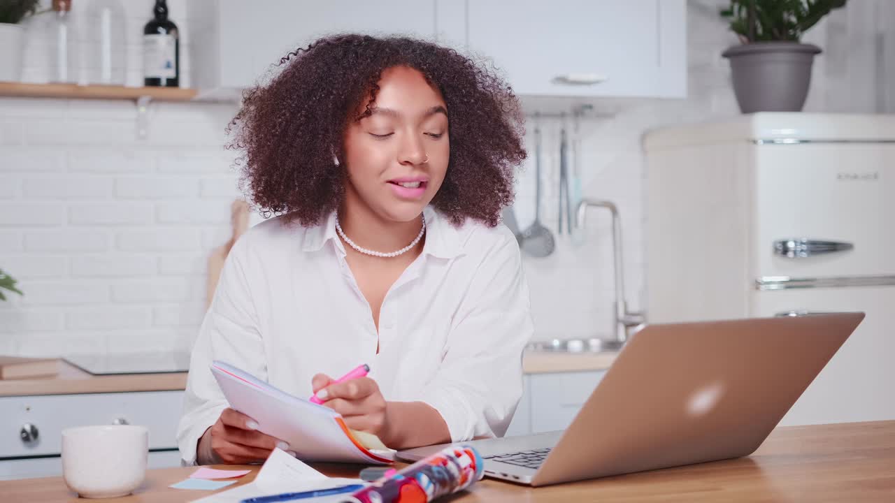 Giovane donna afroamericana seduta in cucina durante una videochiamata al laptop.