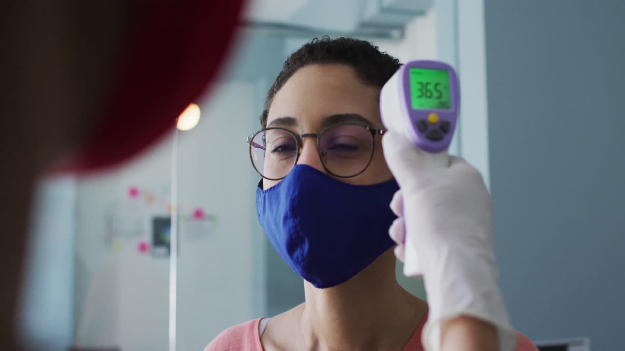 Donna caucasica con mascherina a cui viene misurata la temperatura in un ufficio moderno.