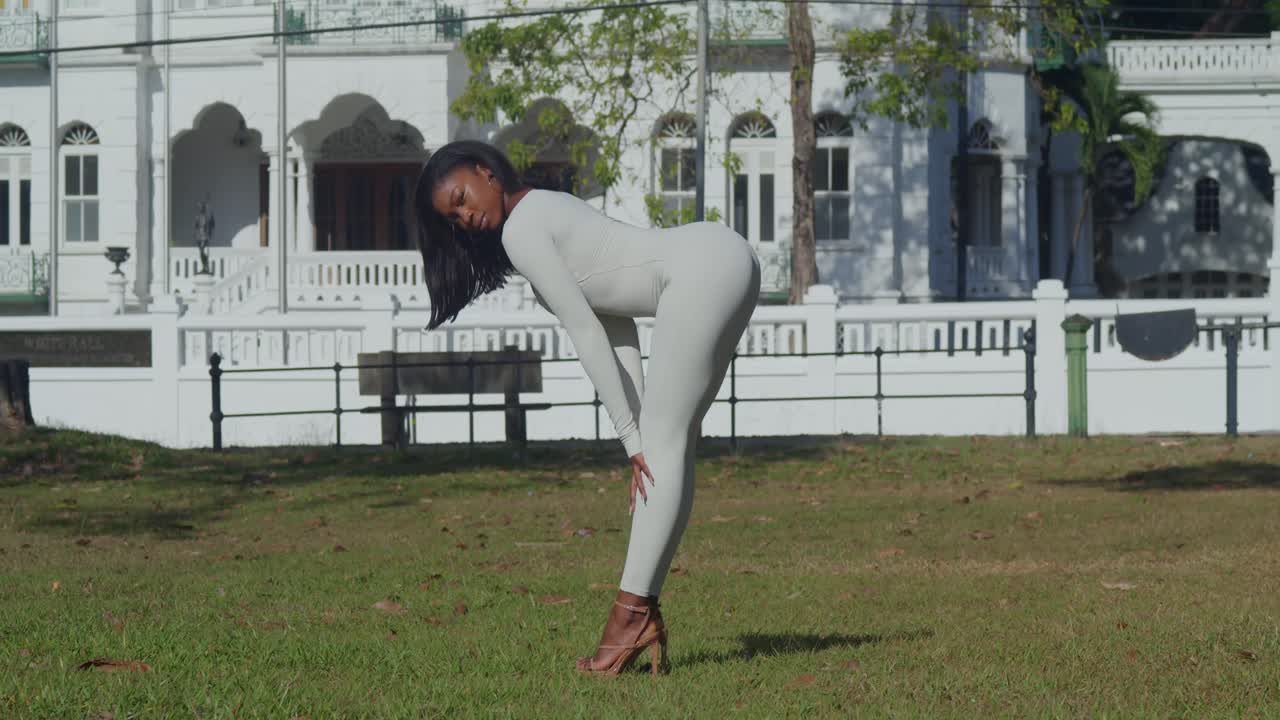 una joven vestida con un bodysuit blanco es vista en una ciudad del caribe, con castillos en la distancia