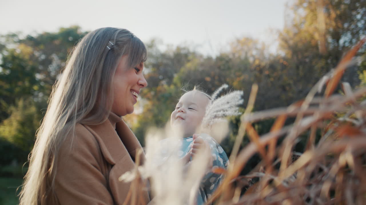 Mom plays with her daughter - shows her the reeds in the park. Have a good time outdoors on a clear autumn day