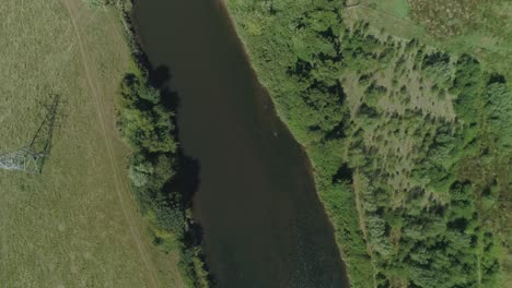 vista aérea sobre un río, rodeado de árboles y zonas verdes, con cables eléctricos desde una torre de transmisión cruzando el agua.