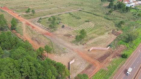 aerial view of a red dirt worksite on farmland in green countryside while machines working on a new subdivision.