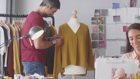 Diseñadores-De-Moda-Masculinos-Y-Femeninos-Sonrientes-Con-Máquina-De-Coser-Trabajando-Juntos-En-El-Estudio