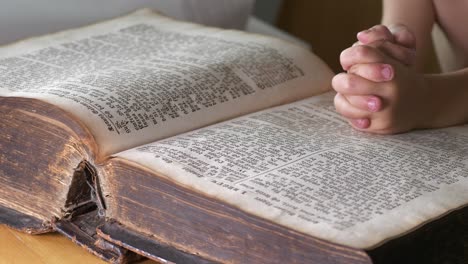 clasped hands of child praying on open old bible book