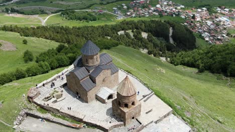 Filmflug-über-Die-Gergeti-Dreifaltigkeitskirche,-Die-Eine-Kleine-Stadt-In-Der-Nähe-Eines-Hügelhangs-Enthüllt