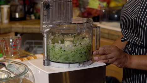 mujer negra mezclando pimientos jalapeños y cebollas en un procesador de alimentos, primer plano