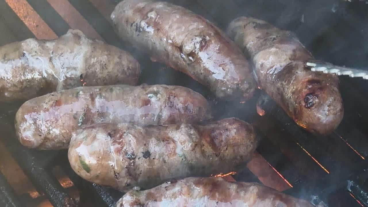 Saporite salsicce sfrigolano ed emanano fumo mentre vengono girate con le pinze su una griglia rovente all'aperto