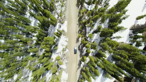 Drone-Se-Aleja-Del-Jeep-Wrangler-Conduciendo-A-Través-De-Montañas-Nevadas,-Viaje-De-Aventura-En-Solitario