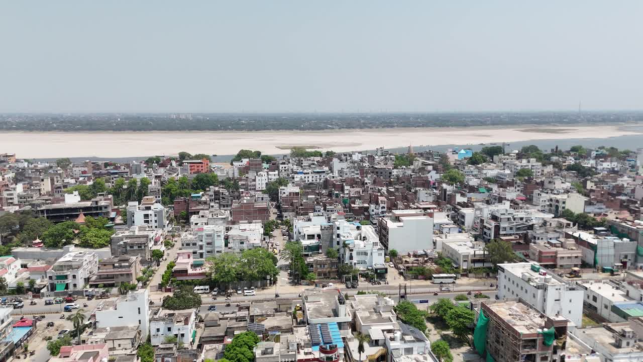 Aerial shot of the sun setting over Varanasi, casting long shadows over the densely packed neighborhoods and historic temples along the Ganges.