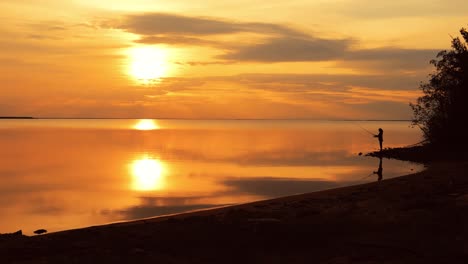 frau fischt auf einer angelstange, die sich im hintergrund beim sonnenuntergang dreht.