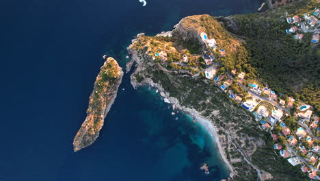 aerial birds eye view over clifftop villas along javea coastline with tilt up reveal of golden sunset on horizon