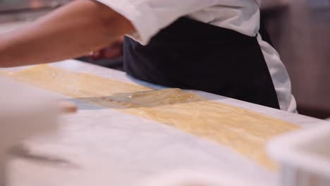 Male-cook-presses-a-scraping-ring-into-the-pasta-dough-in-a-restaurant-kitchen