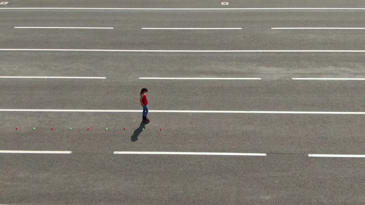 Athlete trains in the open area, goes round the cones, slalom, criss cross. Athlete takes acceleration and goes on roller skates. View from the copter. 4k, 10bit, ProRes