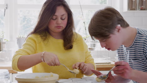 Young-Downs-Syndrome-Couple-Putting-Mixture-Into-Paper-Cupcake-Cases-In-Kitchen-At-Home