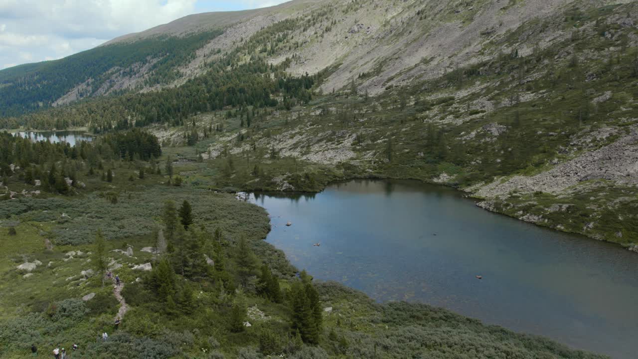 Drone footage of Karakol Lakes surrounded by taiga forest and rocky mountain slopes in Altai Republic, Russia, calm wilderness landscape under cloudy sky