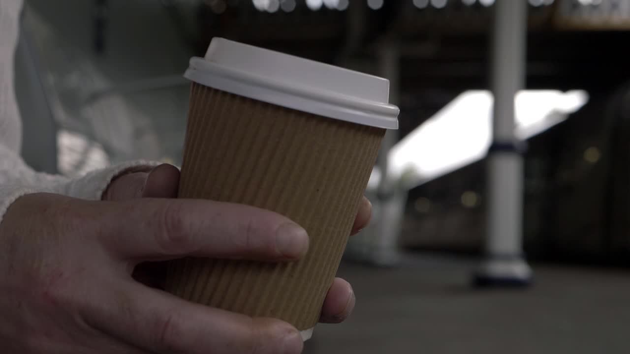 Hands holding takeout coffee as train leaves station