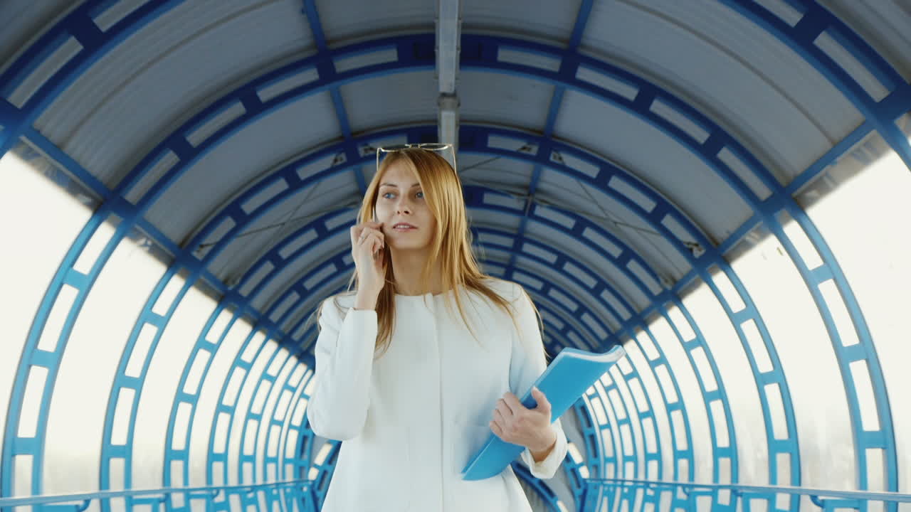 деловая женщина в костюме разговаривает по современному переходу, держа в руках папку с документами и телефон