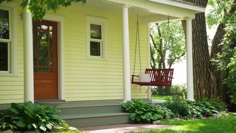 static shot of the front of a farm house with a swing on the porch that is slowly rocking in the wind