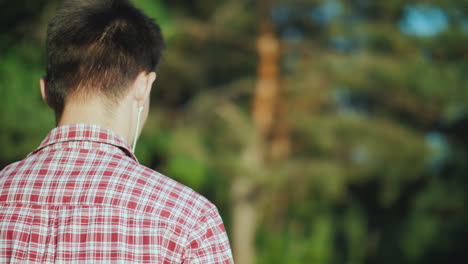 A-Teenager-Walks-In-The-Park-Listening-To-Music-On-Headphones-Rear-View-Video-With-Shallow-Depth-Of-