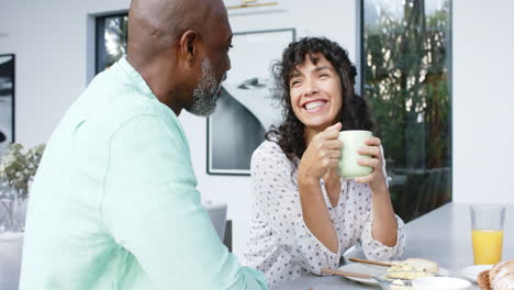 Happy-biracial-couple-having-scrambled-eggs-for-breakfast-and-talking-in-kitchen,-slow-motion