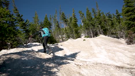 female hiker climbing snow-covered trail with hiking pole and crampons during the spring