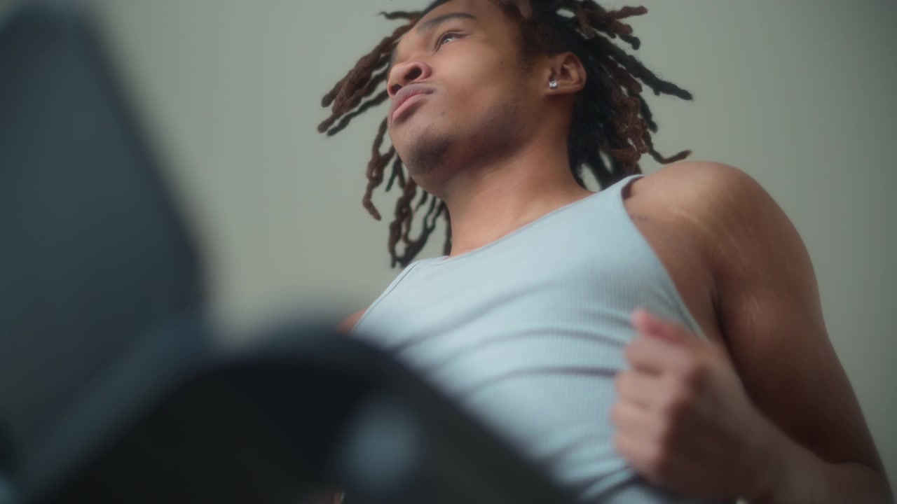 Lavvinkelbillede af en ung mand med dreadlocks på et løbebånd