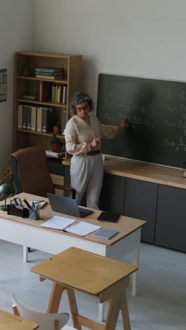Teacher explaining math formulas on a chalkboard in a classroom