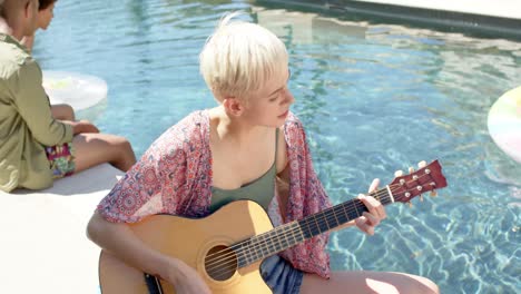 Happy-diverse-group-of-friends-playing-guitar-at-pool-party-in-summer