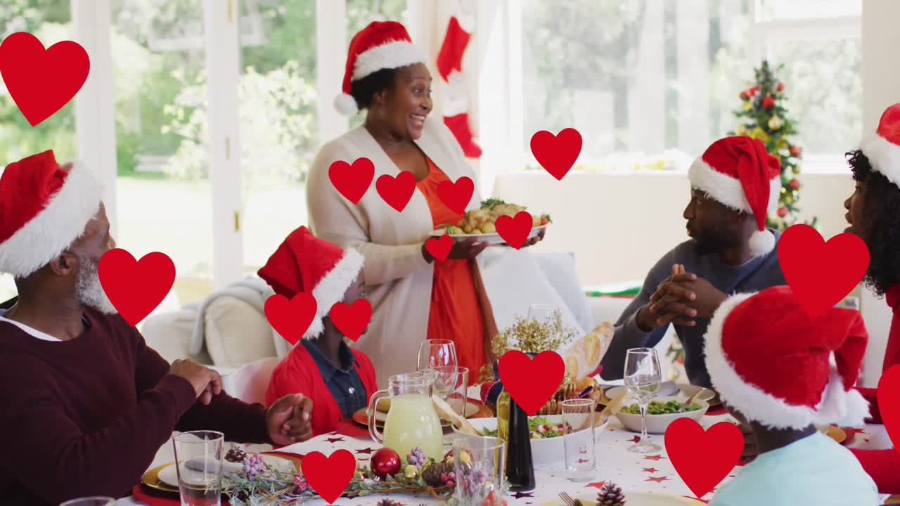 animación de corazones flotando sobre una feliz familia afroamericana durante la cena de navidad
