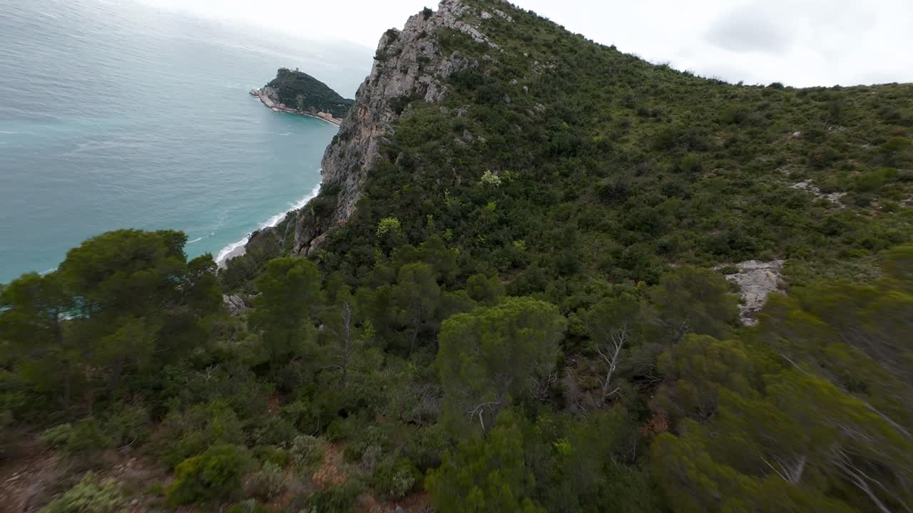 FPV drone flies over rugged coastal cliffs and green vegetation with ancient ruins overlooking the sea near Noli, Liguria, Italy. Aerial