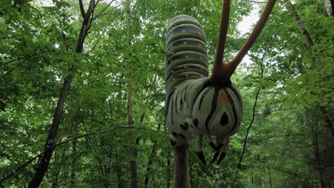 Gran-Modelo-De-Oruga-Contra-Los-árboles-Verdes-En-El-Bosque-En-El-Parque-De-Gigantes-Kashubian,-Strysza-Buda,-Polonia