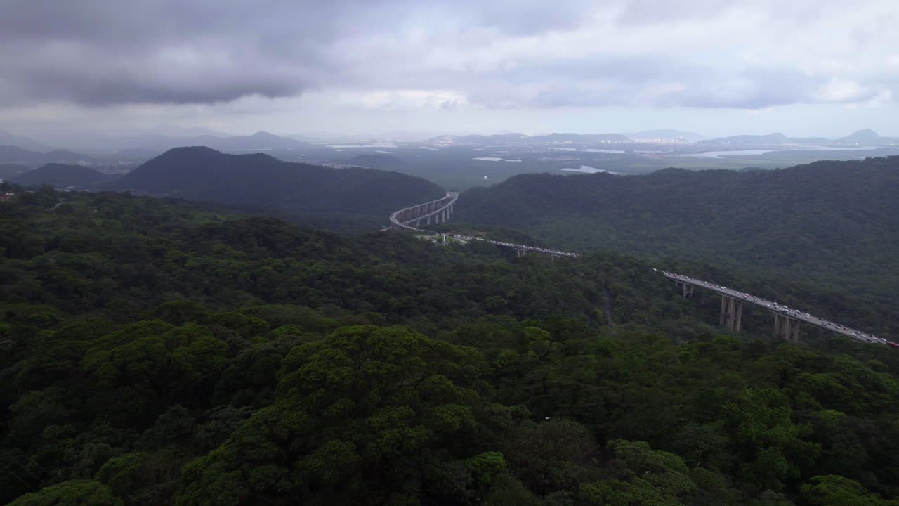 Aerial view flying over forest towards the Santos highway in Mata atlantica, cloudy Brazil